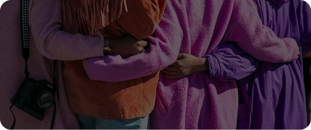 Close-up of people wearing colorful clothing, standing side by side with arms around each other in a show of support and unity